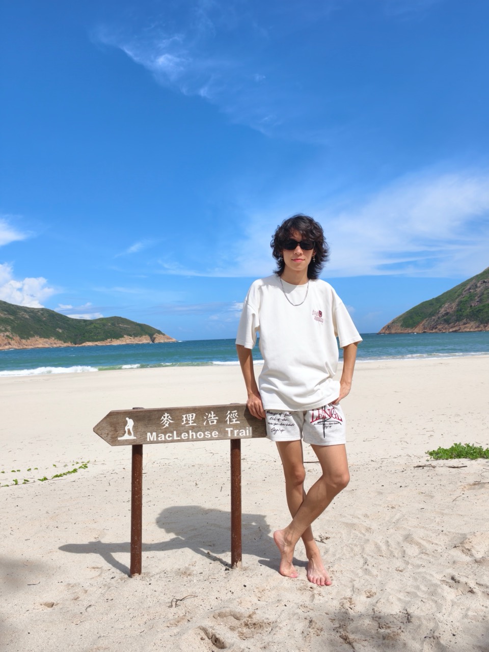 Sam standing beside the MacLehose Trail sign on a sunny beach.